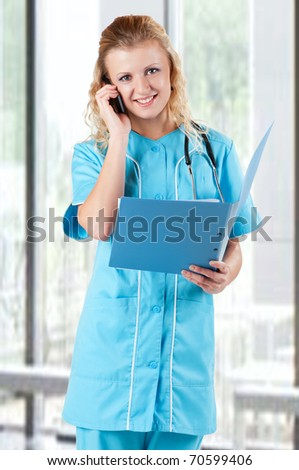 Beautiful young doctor with file folder holding a mobile in hospital