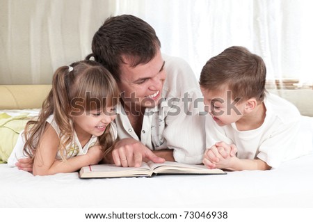 Lovely family - father with children, reading a book, on the bed