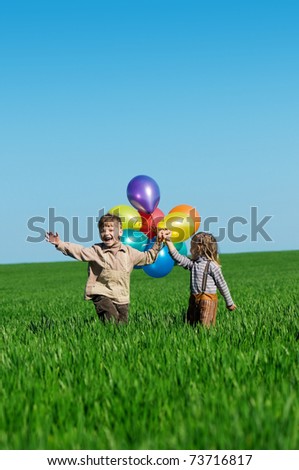 Happy sister and brother with balloons walking on the spring field