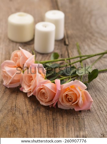 Lying down roses with white candle over wooden
