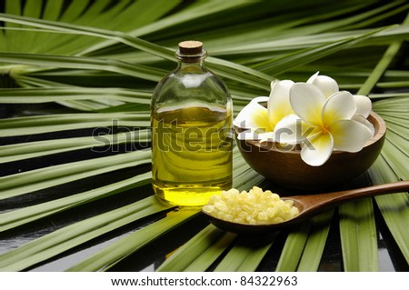 Frangipani flower in bowl and massage oil and bath salt in wood spoon on palm leaf