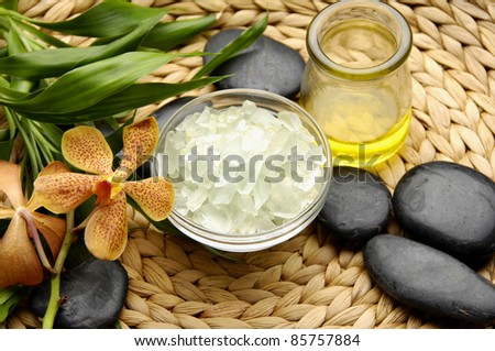Bowl of slat and and massage oil with orchid with bamboo leaves on woven wicker mat