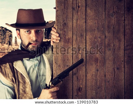 Bad gunman in the old wild west indicates with the gun a wooden plank