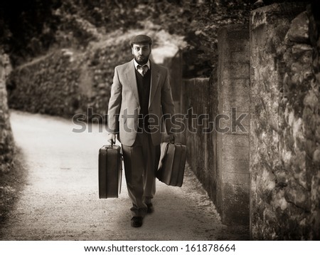 Emigrant man with the suitcases in a narrow country
