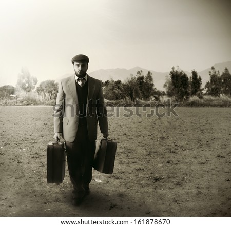 Emigrant man with the suitcases in an agricultural field