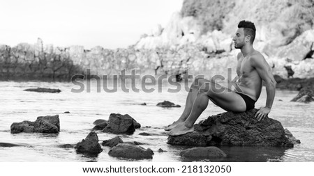 Young handsome muscular man in swimsuit on the stony beach.
