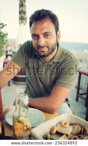Young man enjoying a drink sitting at the restaurant near the sea.