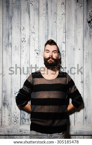 Hipster man with big beard and moustaches stands near the white wooden wall