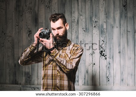 Bearded man holds a vintage film camera. Shot on pale wooden background.