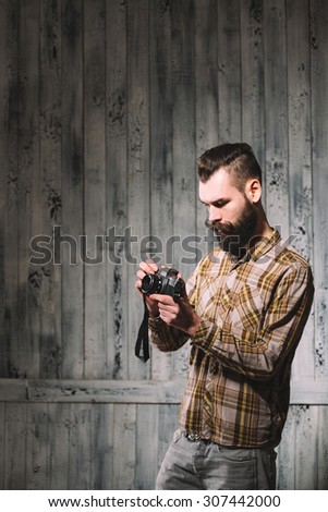 Bearded man holds a vintage film camera. Shot on pale wooden background.