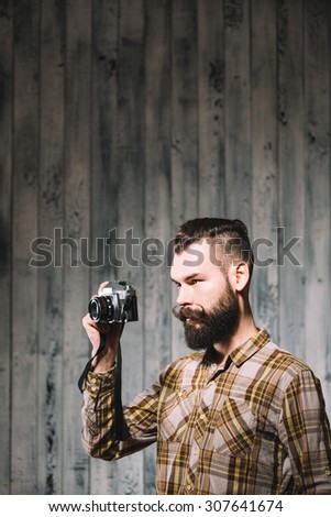Hipster man shoots with a vintage film camera. Shot on pale wooden background.