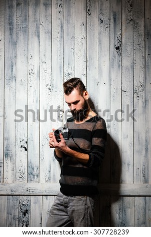 Bearded man holds a vintage film camera. Shot on bright white painted wooden background.