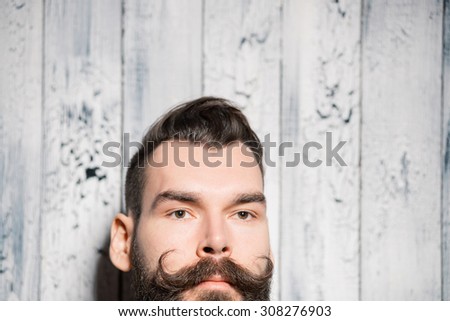 Man with big curved mustache, close-up portrait on pale white painted wooden background. Shallow depth of field.