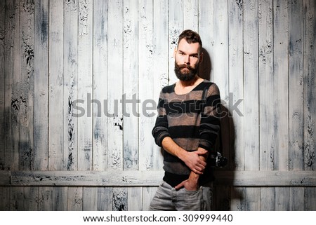 Man with big beard and huge mustaches stands in front of the white-painted wooden wall.
