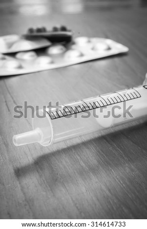 Monochrome medicines and syringe on a wooden table.
