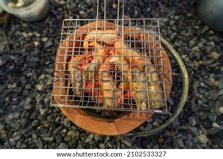 Thai river prawns grilled over charcoal grill Grilled on a BBQ Thai iron grill . Giant grilled lobster cook on charcoal stove at Thai street food night market. Grilled Giant River Prawn.