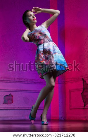 Full length portrait of a beautiful young girl wearing colorful dress and high heel shoes, with bright make up posing looking aside, standing in a purple room