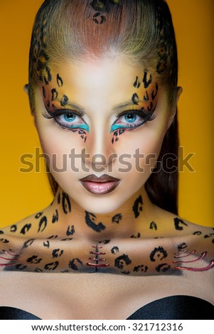 Close up portrait of a young woman with leopard make up on her face, looking at the camera, isolated on yellow background