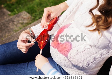 Love concept. Husband and wife in expectation on childbirth. Pregnant woman. Happy pregnancy. Big pregnant belly of woman. Heart shape made by lollipops . Happy people.