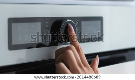 Female finger is touching the button of modern panel of electric oven. Technology concept. Focus to the female finger. Woman using electric oven.
Woman chooses cooking modes in an electric oven