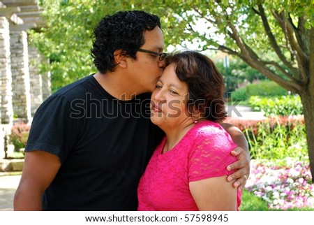 A Hispanic man kisses his mother on the forehead