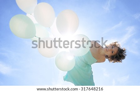 young woman in a dress holding balloons against sun