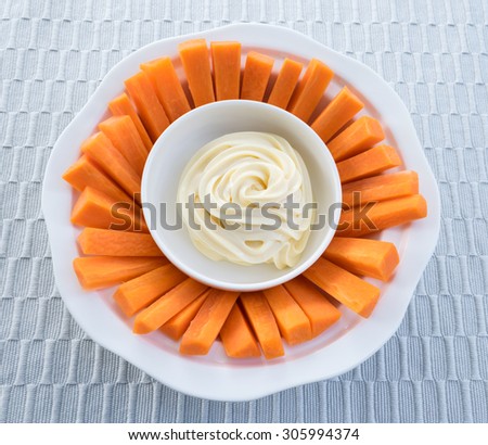 carrot sticks with mayonnaise on white plate placed on a gray tablecloth background.