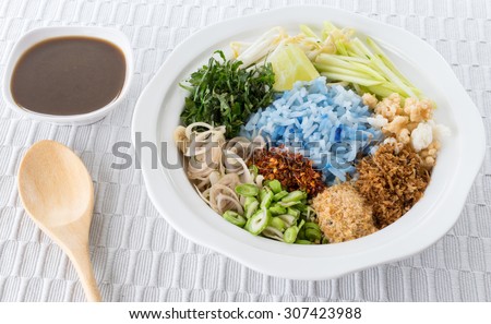 Thai cuisine , Thai Southern food, Spicy blue rice salad with mix vegetable on white plate, placed on a gray tablecloth background.