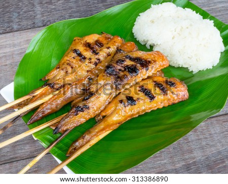 Thai cuisine, Grilled chicken wings, with sticky rice on white plate with green leaf, place on wooden table