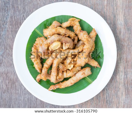 Fried pork with garlic, fried pork cut into piece, on white plate with green leaf, place on wooden background, top view