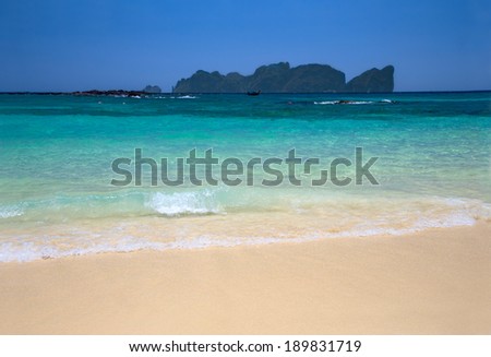 Tropical white sand beach with  turquoise water and an island on the background