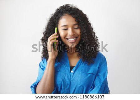 Joyful beautiful young Afro American female with black curly hair smiling happily while talking on mobile, receiving good news. Attractive mixed race girl having nice phone conversation n studio Foto stock © 