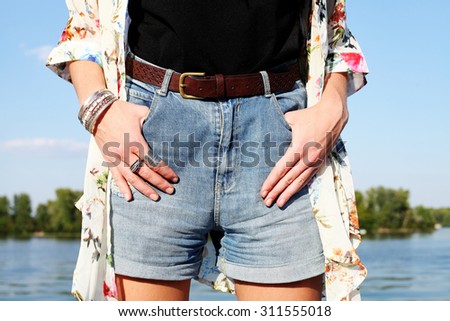 stylish girl in denim shorts with a high waist. hands with bracelets and rings close up. boho chic vintage outfit