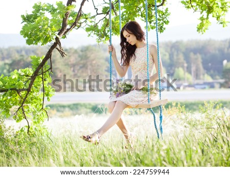 Young woman is swinging on a swing in summer forest.
