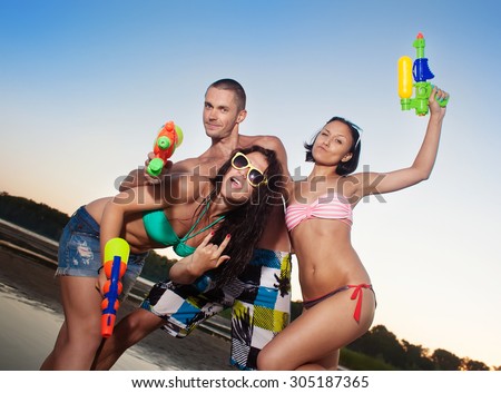 Group of young joyful young people playing with water pistols on the beach