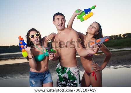 Group of young joyful young people playing and posing with water pistols on the beach