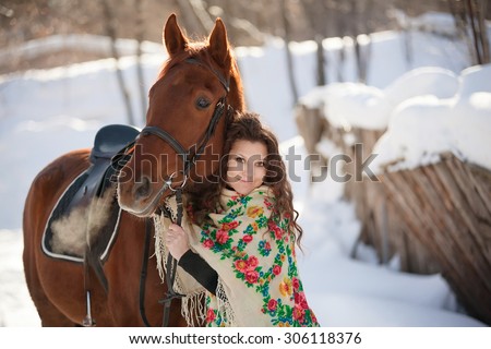 beautiful young woman in Russian national scarf with a horse in the countryside in winter