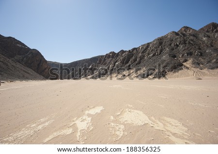View down a dry wadi desert river valley in barren arid climate with mountains