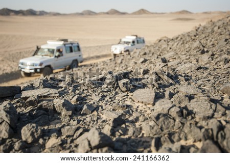 Two off road vehicles driving through a desolate arid rocky desert landscape