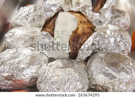 Closeup of baked jacket potatoes in silver metal foil with white sauce at a hotel restaurant buffet