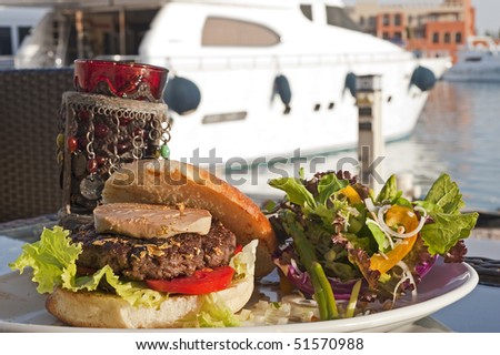 Luxury beef burger with fois gras and gold leaf in a bread bun with private boat in the background
