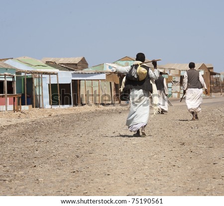 Three local egyptian men walking up dirt road in a rural african settlement