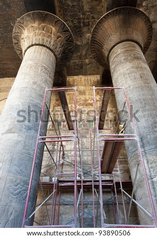 Columns in the ancient egyptian temple of Khnum at Esna with hieroglyphic carvings and scaffolding for restorations