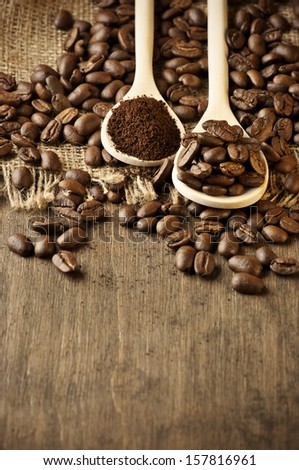 Roasted coffee beans and ground coffee in wooden spoons on coffee heap.