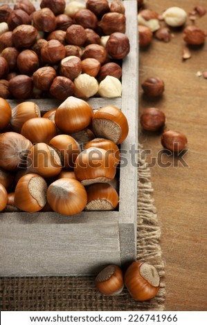 Whole and peeled hazelnuts in wooden box on burlap and wood.