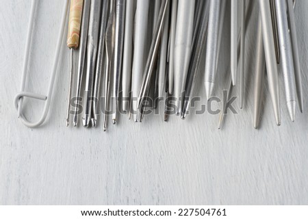 Set of vintage gray metallic knitting needles and crochets on rustic wooden table close-up. Shallow DOF.