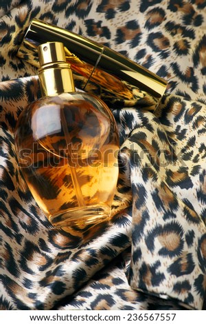 Bottle of woman perfume and gold lipstick on animal style headscarf.