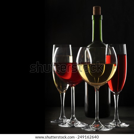 Various glasses of red and white wine with abstract pattern and bottle on black wooden background.