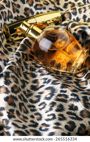 Bottle of woman perfume and gold lipstick on animal style headscarf.
