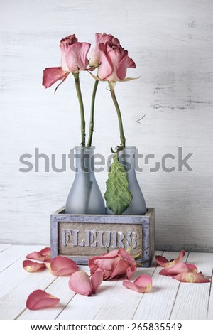 Wilted roses in rustic vase and fallen petals on wooden background. Vintage stylized, filtered image.